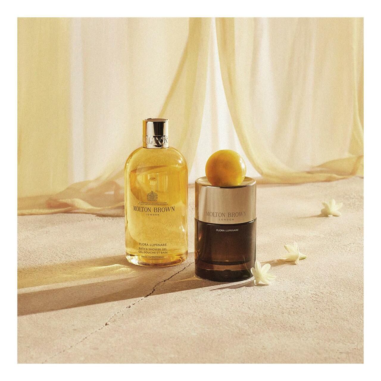 Due flaconi e una sfera su una superficie. Scritta: Molton Brown. Fiori bianchi sparsi.