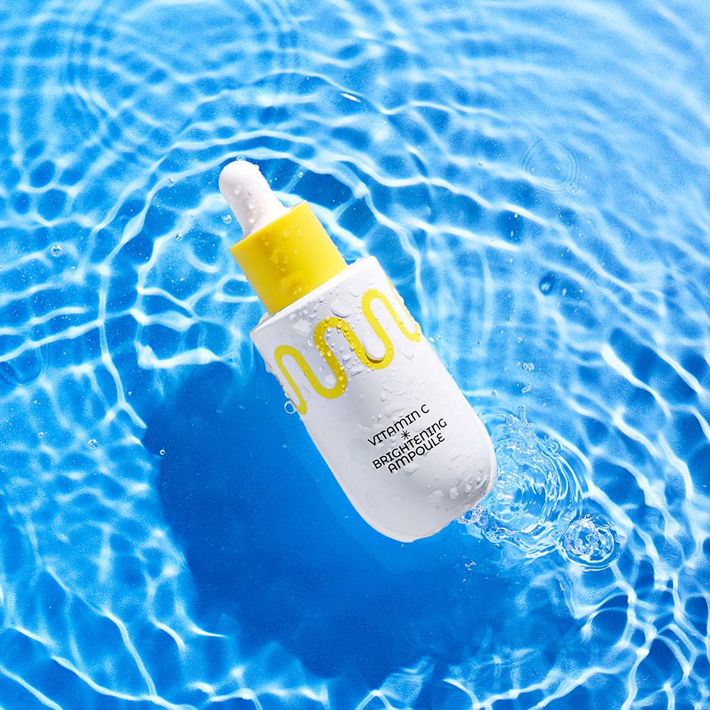 Flacone contagocce bianco con tappo giallo, circondato dall'acqua. Contiene Vitamin C Brightening Ampoule.