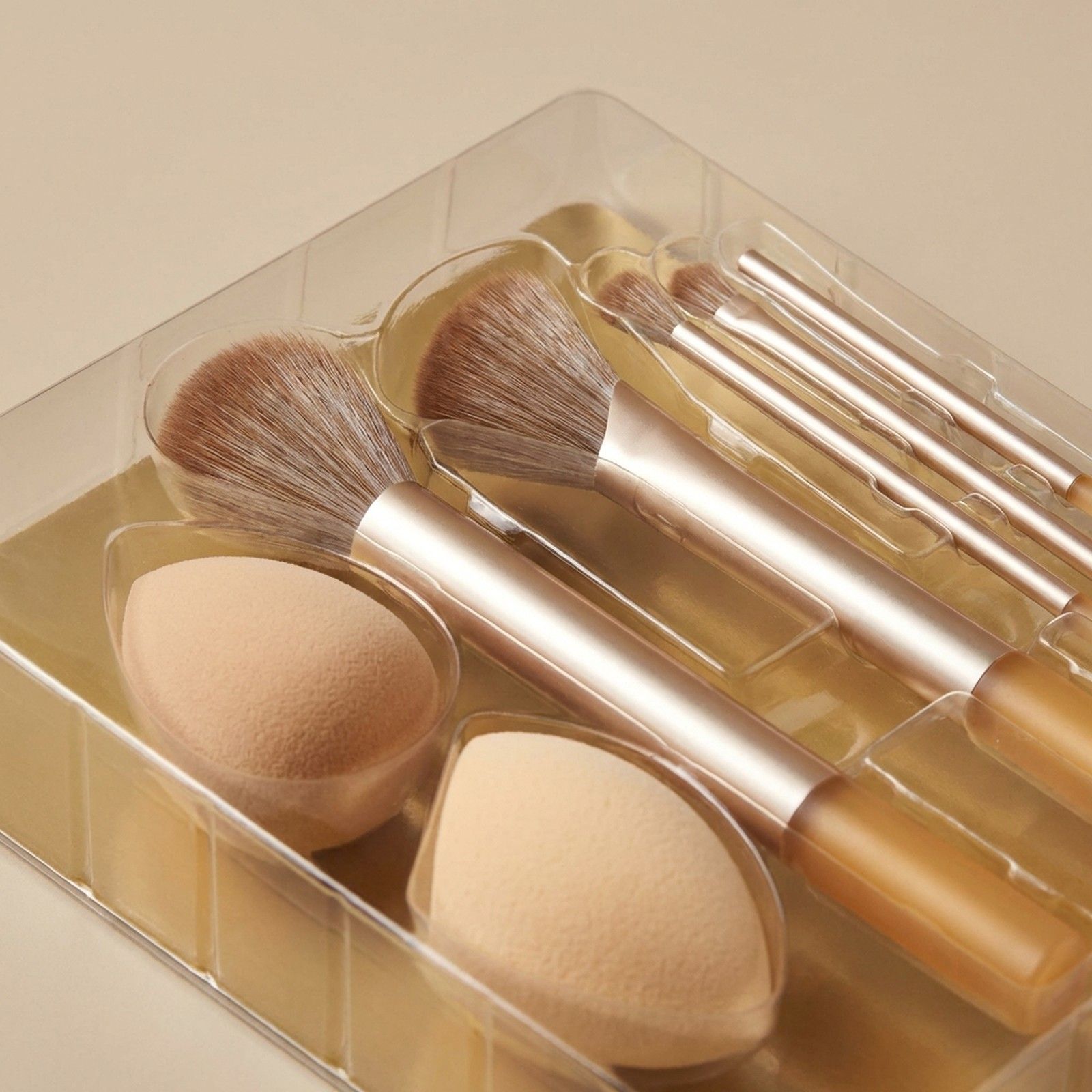 Set di pennelli e spugnette per il trucco in confezione trasparente. Manici dorati, setole marroni.