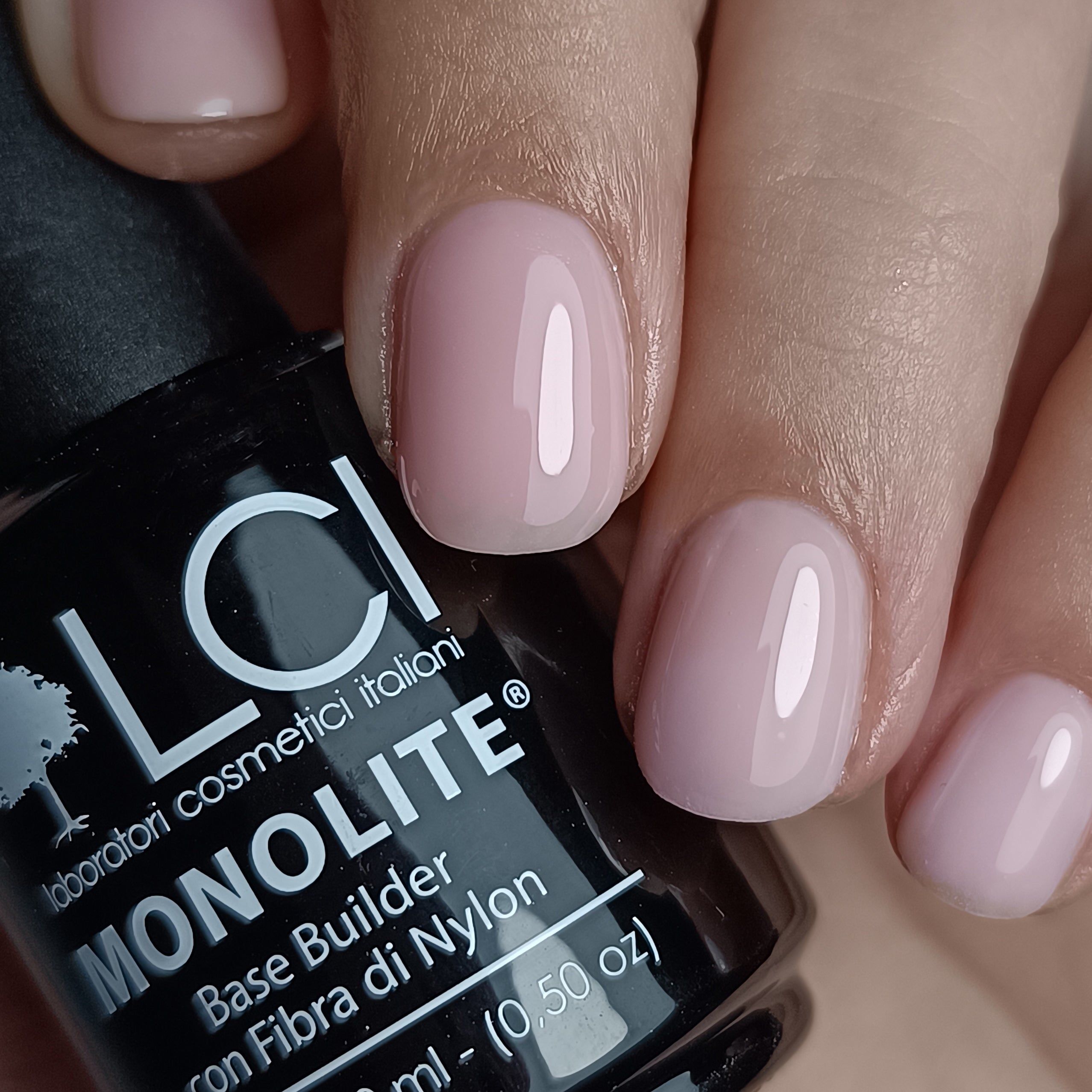 Mano con unghie smaltate rosa chiaro. Accanto, un flacone nero con la scritta LCI MONOLITE.