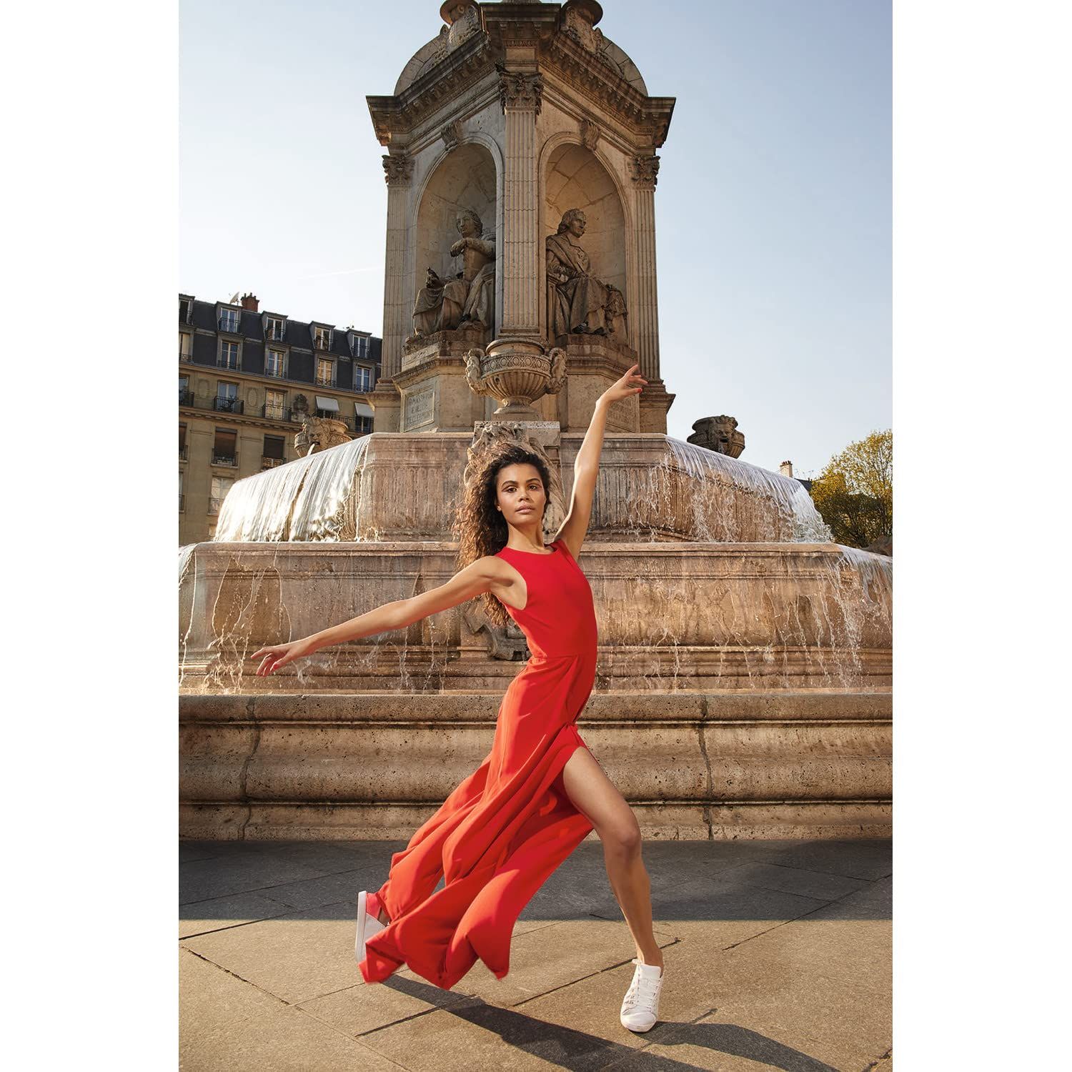 Ballerina in abito rosso davanti a una fontana. Posizione di danza, braccia tese.