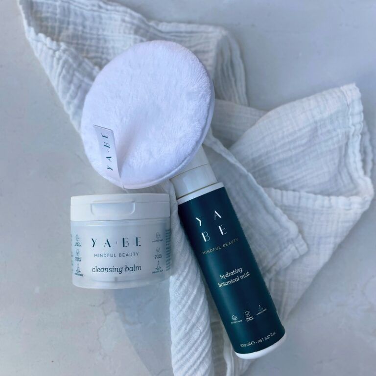 Vasetto bianco con coperchio. Scritta: YA.BE, Mindful Beauty, Cleansing Balm. Accanto a flacone spray e dischetto.