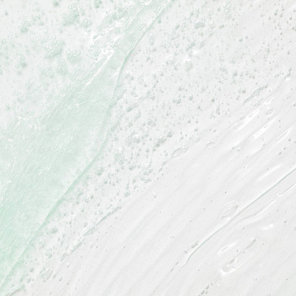 Una texture gel trasparente verde pallido con piccole bollicine d'aria, distribuita su una superficie bianca.