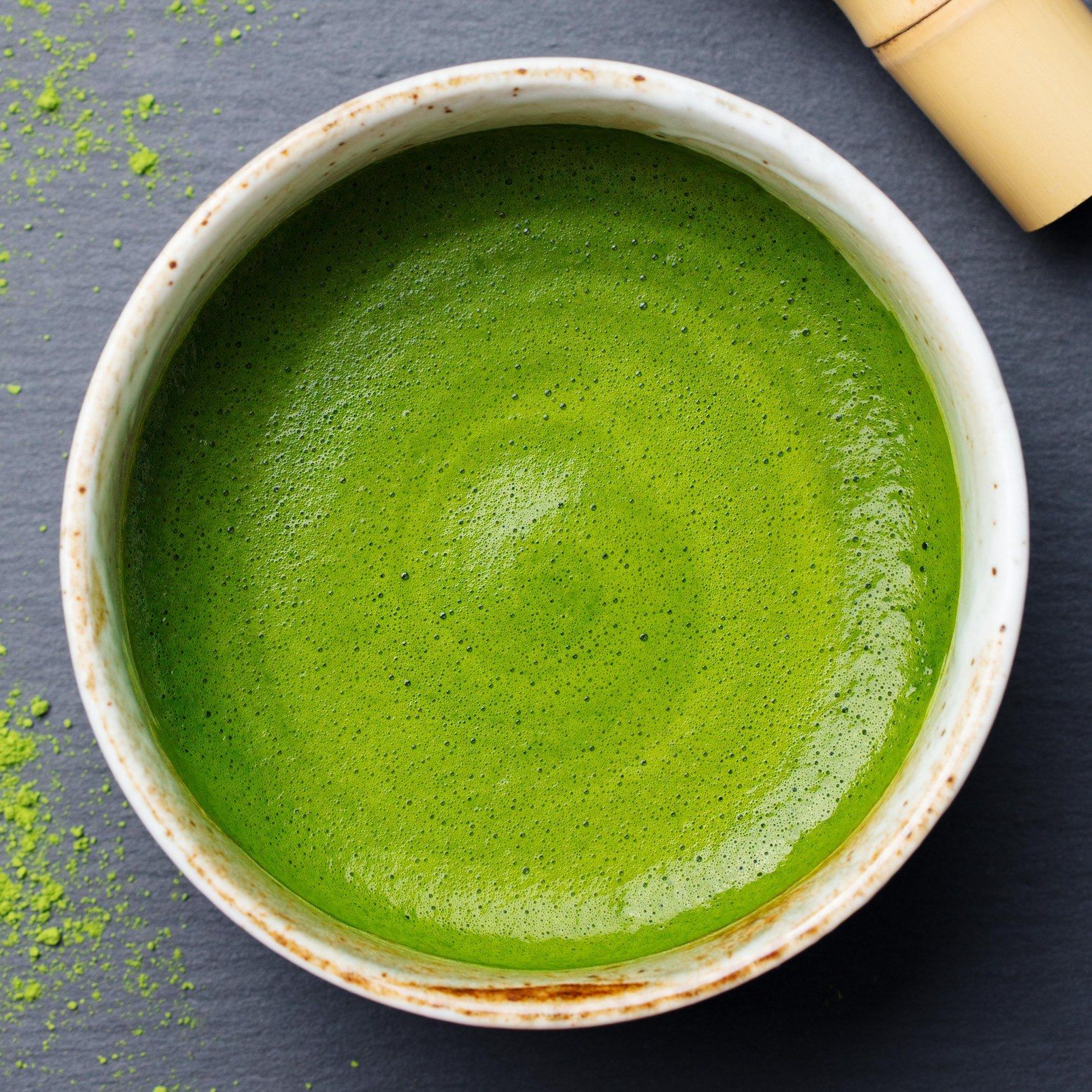 Una ciotola di tè matcha sbattuto. Il tè è verde chiaro e schiumoso. Accanto c'è una frusta di bambù.