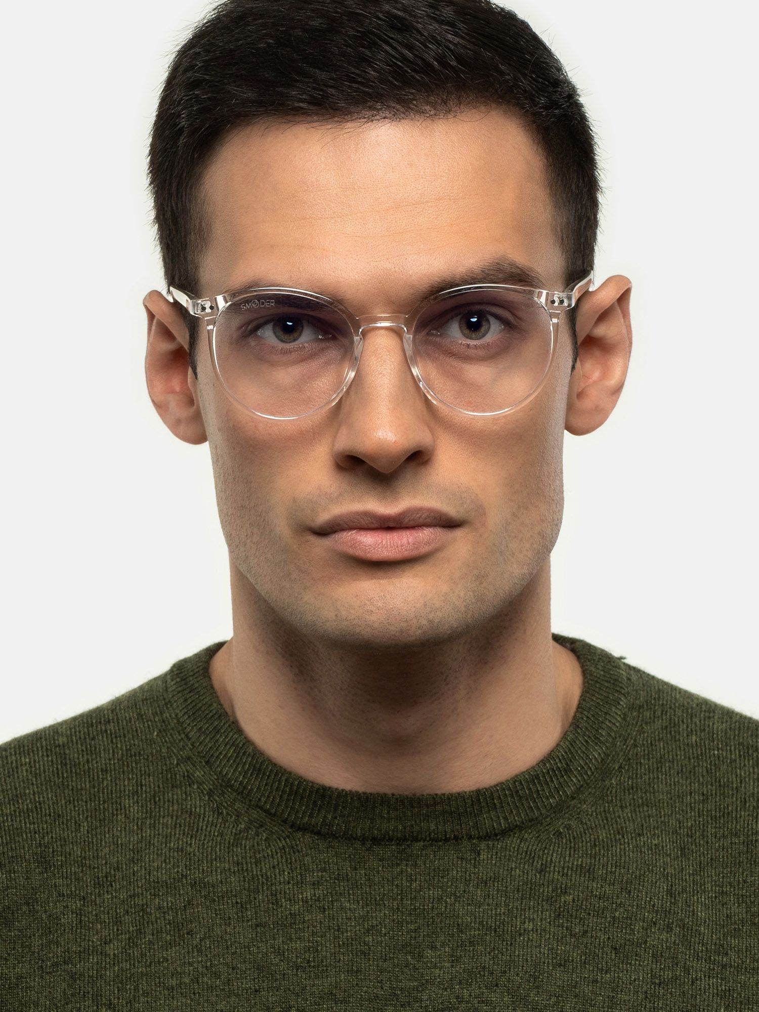 Uomo con occhiali trasparenti. Montatura rotonda, trasparente. Maglione verde.