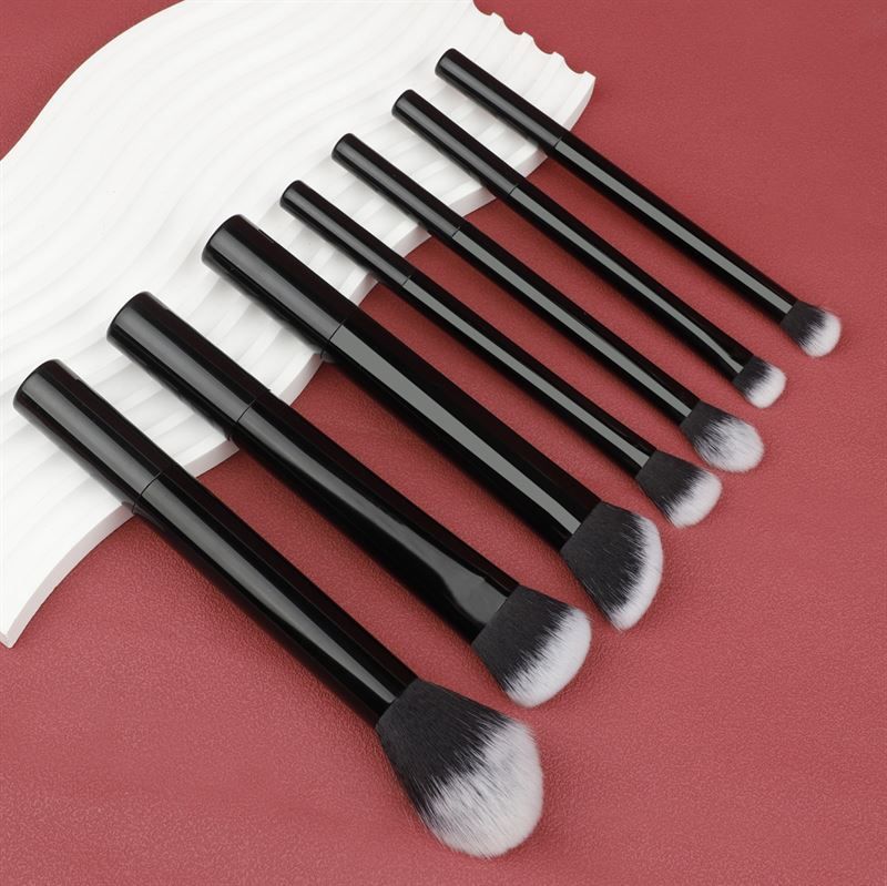 Sette pennelli per trucco neri con setole bianche, disposti su sfondo rosso. Diverse forme.