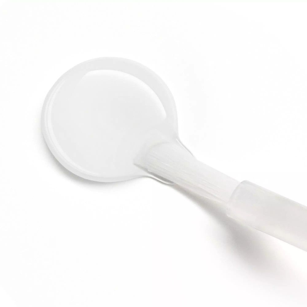 Liquido trasparente su una superficie rotonda con pennello. Il pennello è bianco e ha un manico trasparente.