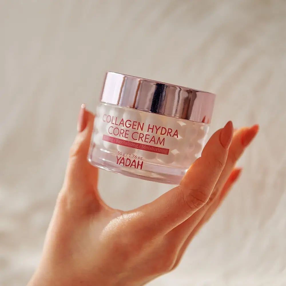 Vasetto di vetro con coperchio rosa. Scritta: Collagen Hydra Core Creme. Marchio: YADAH. Mano che tiene la crema.