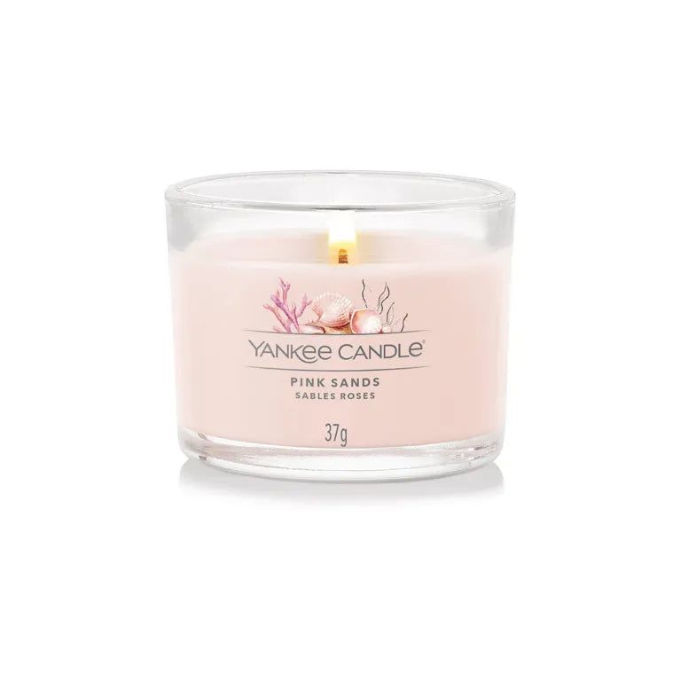 Candela rosa in vetro. Scritte: Yankee Candle, Pink Sands, Sables Roses, 37g. Fiamma accesa.