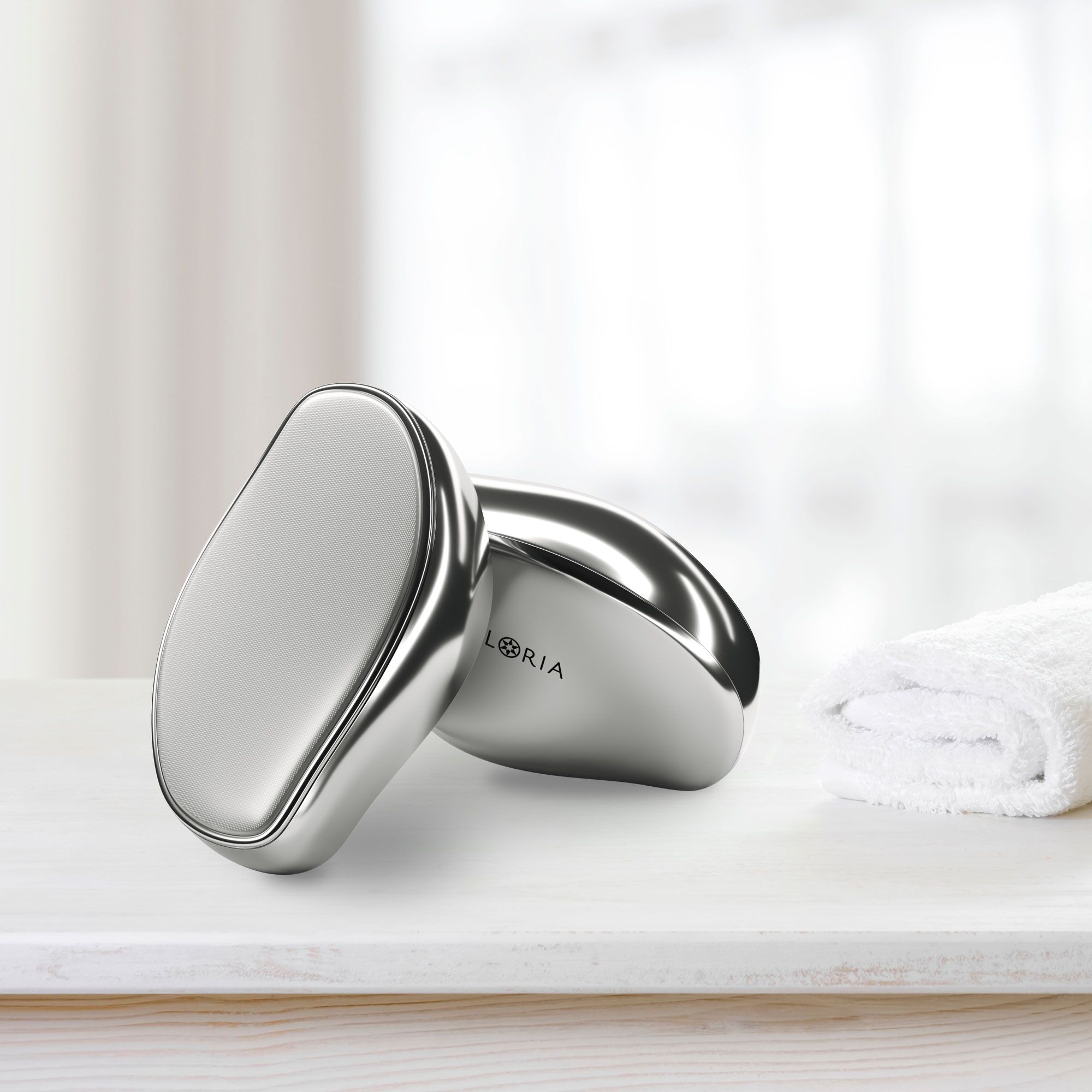 Due dispositivi ovali argentati su una superficie bianca. Un asciugamano bianco accanto. Il nome AILORIA è visibile.