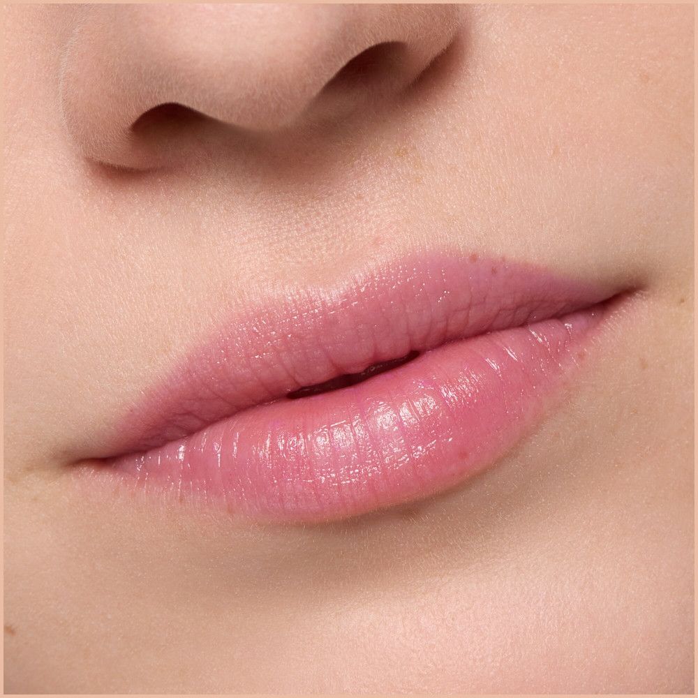 Primo piano di labbra coperte da un balsamo per labbra rosa. Le labbra sono lucide.