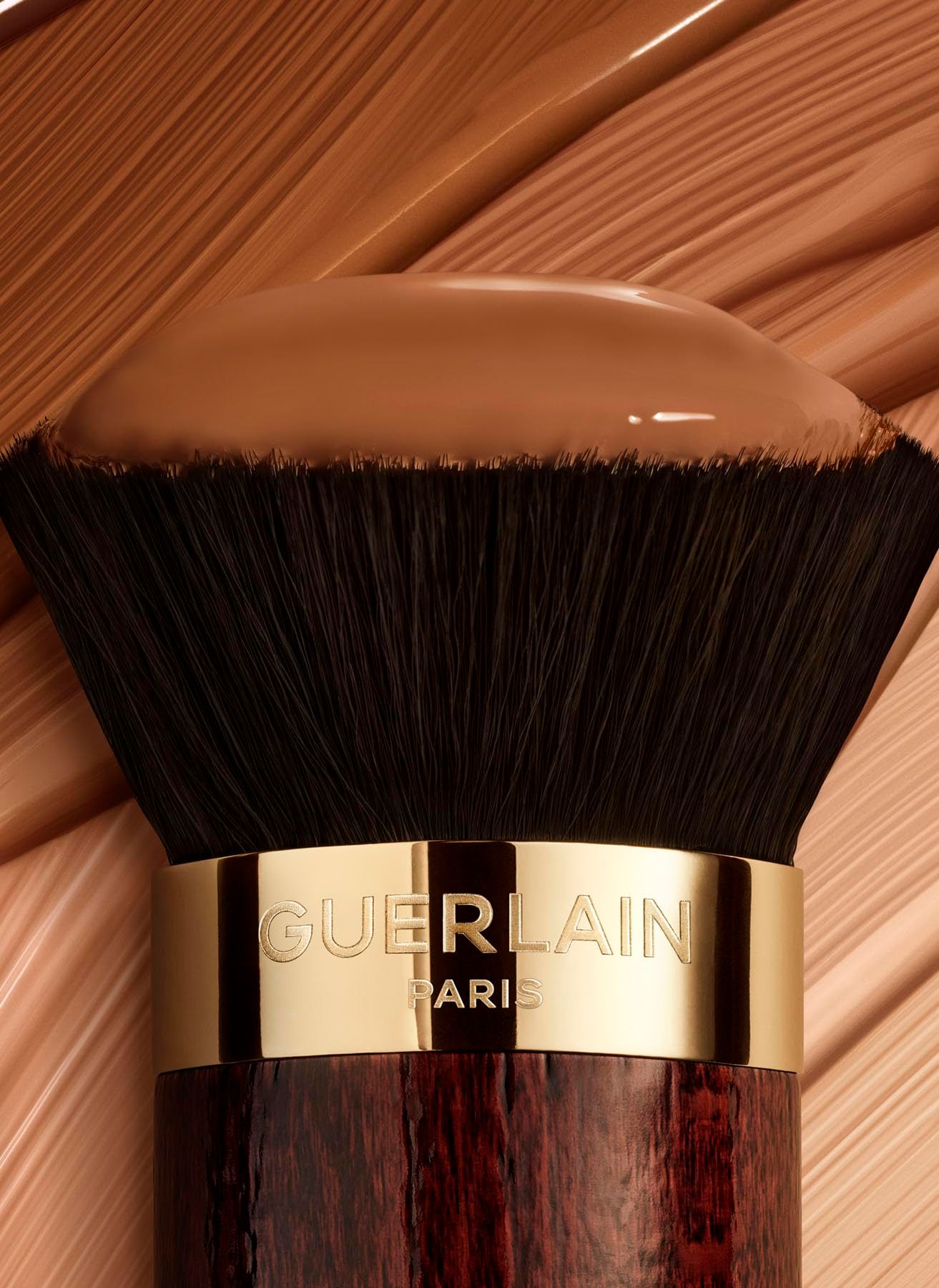 Pennello Kabuki con prodotto trucco sulle setole. Ghiera dorata con scritta "GUERLAIN PARIS".