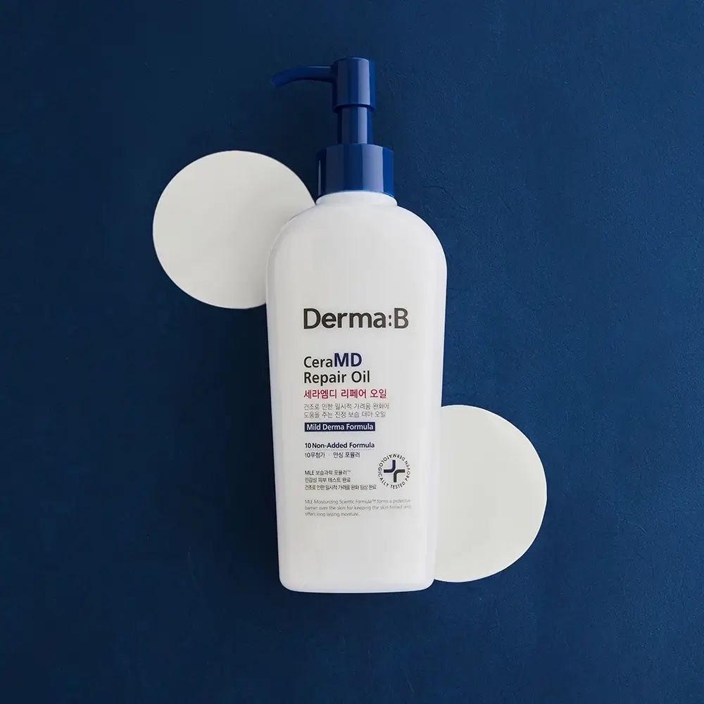 Flacone bianco con erogatore blu. Scritta Derma:B CeraMD Repair Oil. Due cerchi bianchi accanto al flacone.