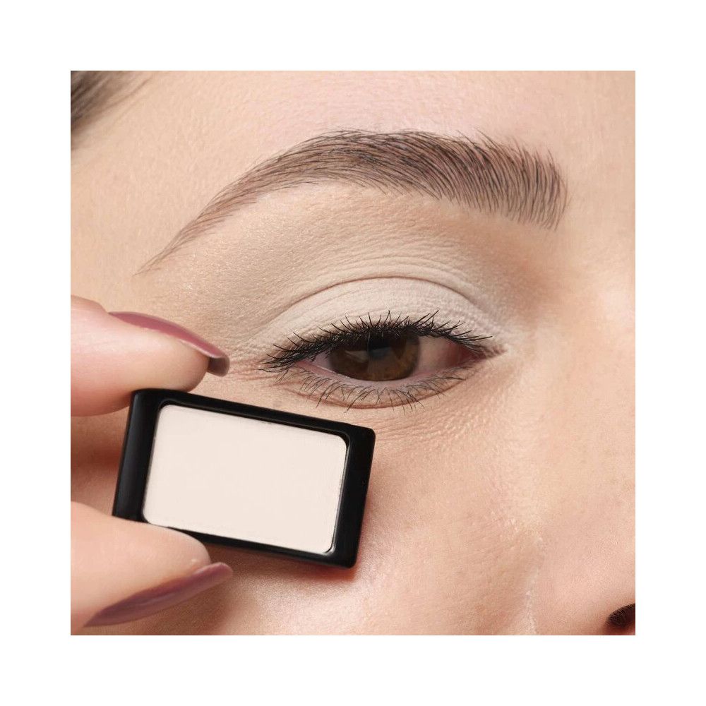 Ombretto in confezione bianca e nera, tenuto in mano vicino a un occhio. Nome del prodotto non visibile.