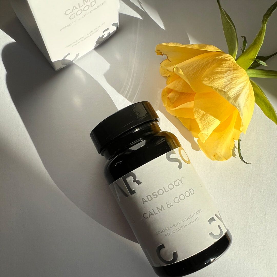 Flacone nero con etichetta bianca. Scritta: Absology Calm & Good. Appoggiato accanto a scatola e rosa gialla.