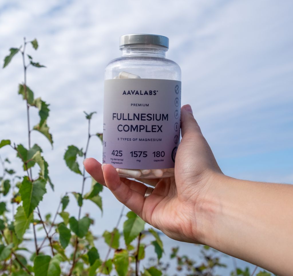 Mano che tiene un flacone di Fullnesium Komplex. Sfondo: natura, cielo blu. 180 capsule.