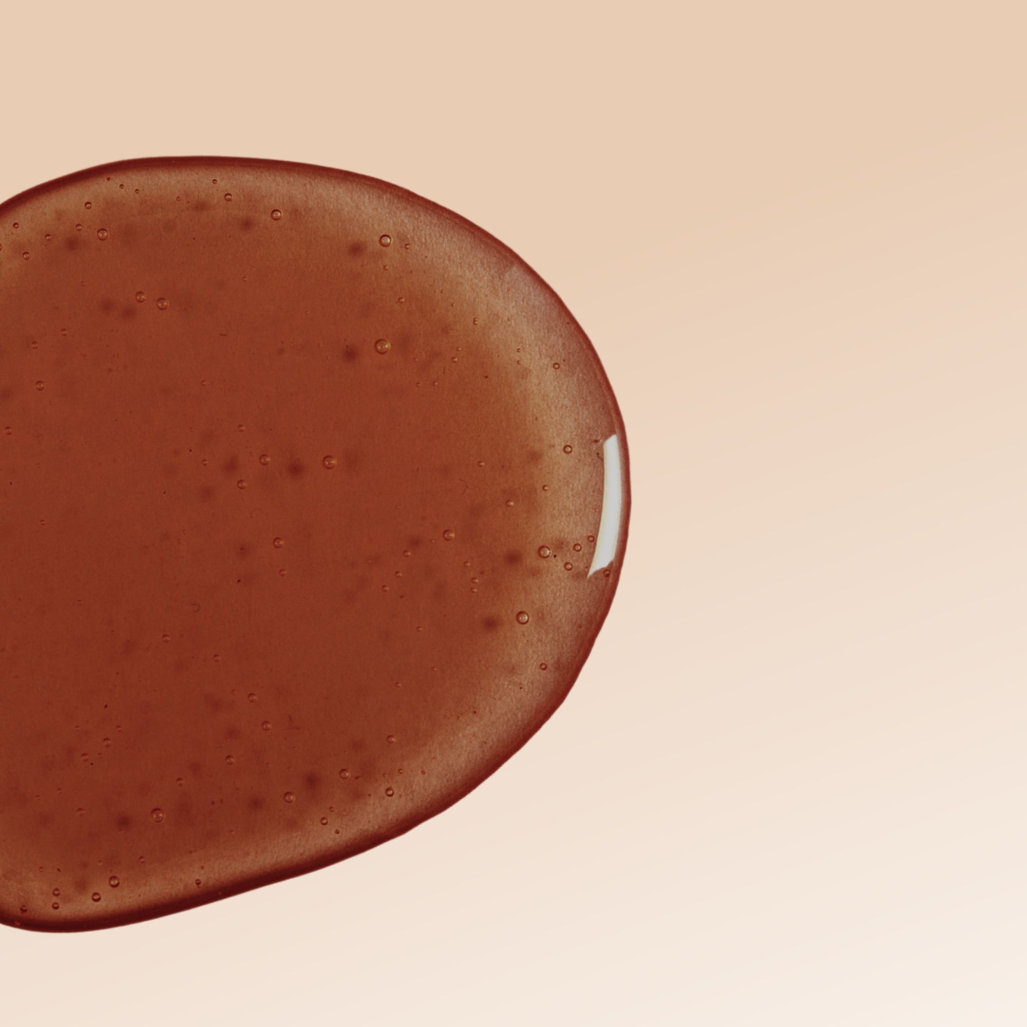 Liquido marrone a forma di goccia su sfondo beige. Bolle visibili.