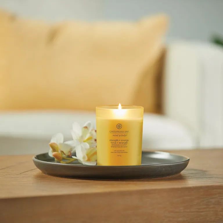 Candela gialla accesa su un vassoio con fiori. Testo: Chesapeake Bay, mind & body, strength + energy, 250 g.