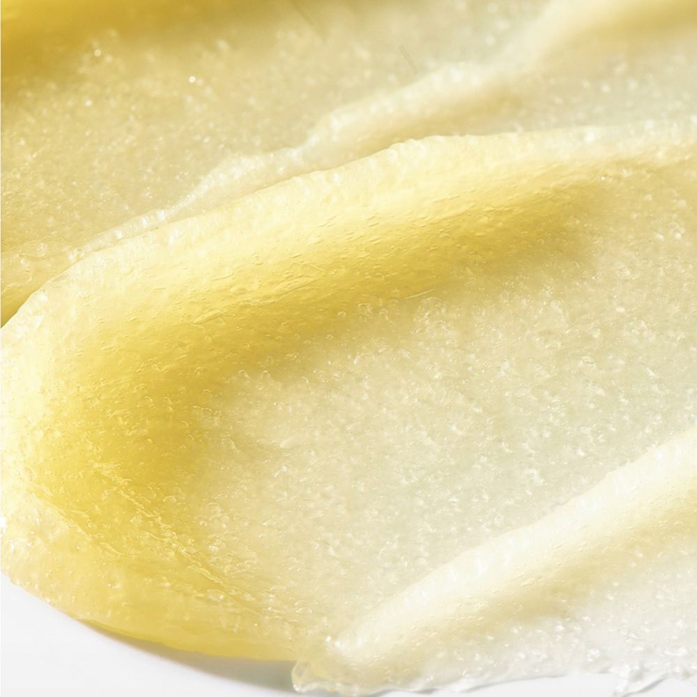 Primo piano di una sostanza cremosa gialla con consistenza granulosa. Su sfondo chiaro.