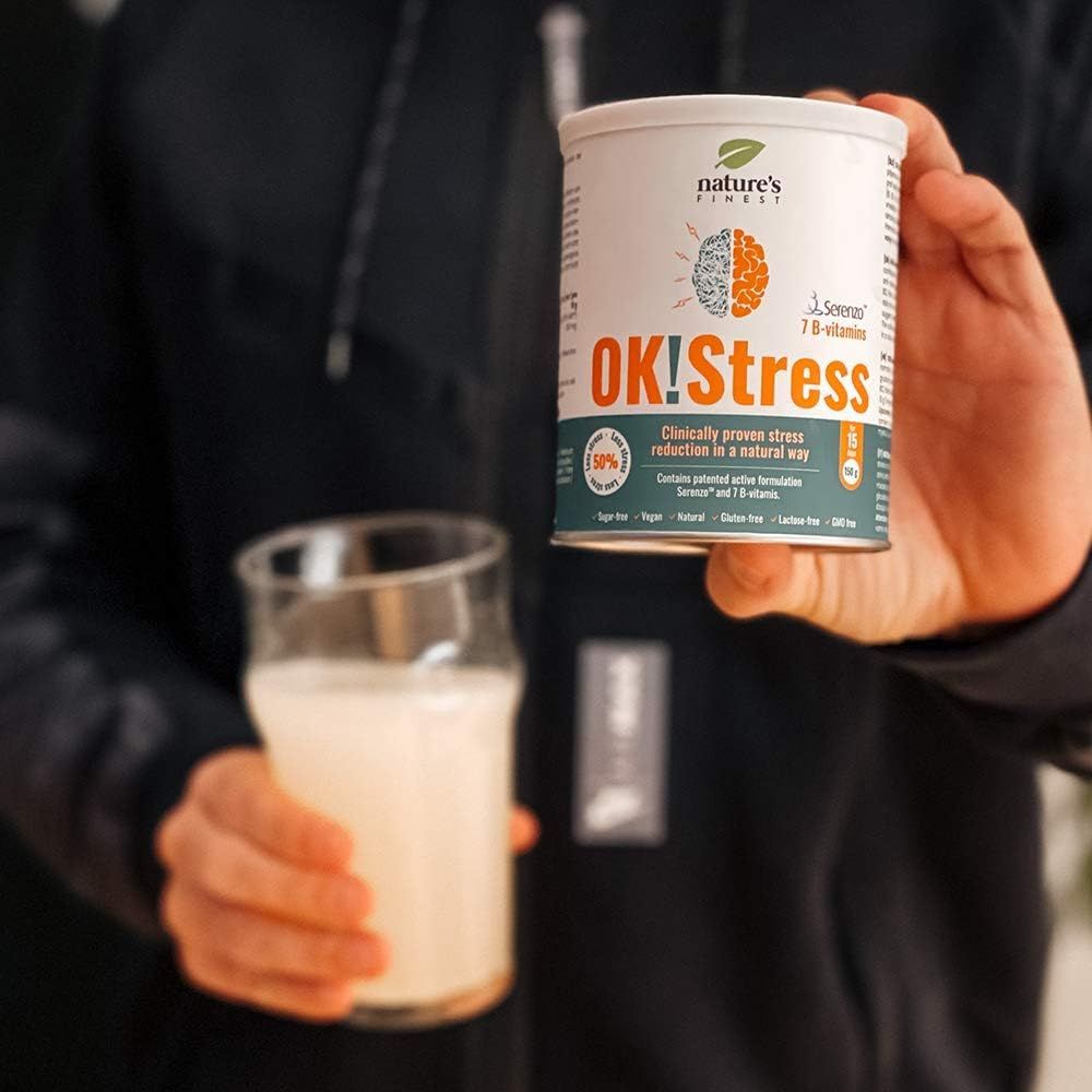 Persona che tiene in mano barattolo OK!Stress e bicchiere. Scritte: Nature's Finest, OK!Stress, 7 vitamine B. Riduzione stress clinicamente provata.