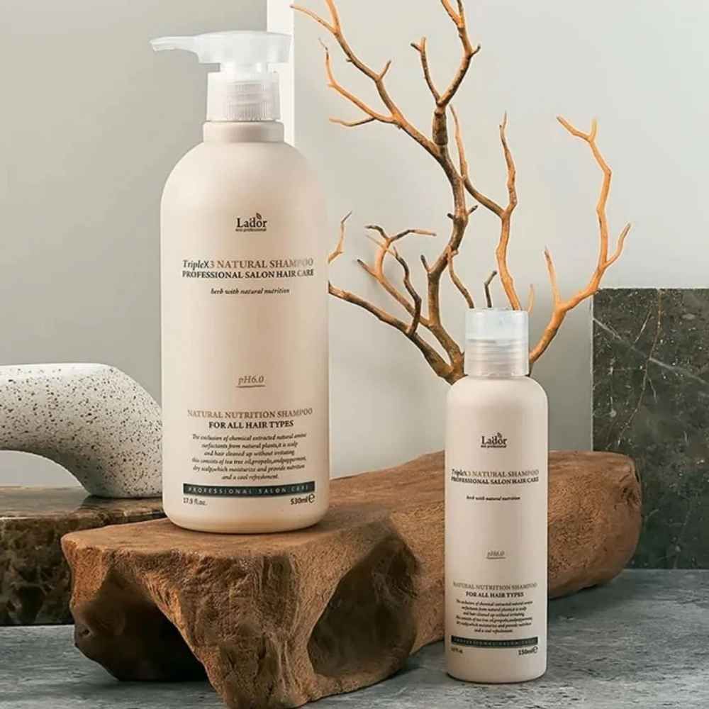 Due flaconi TripleX3 Natural Shampoo, cura professionale dei capelli, disposti su legno e pietra.