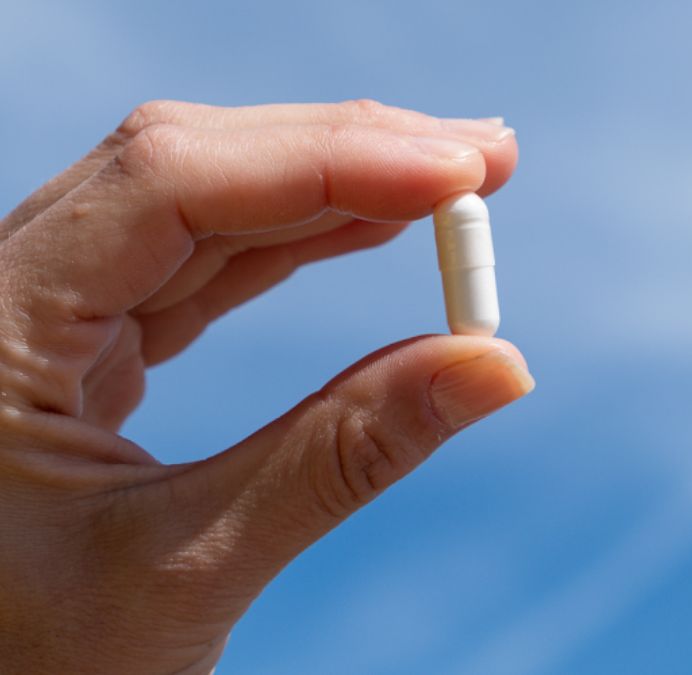 Dita che tengono una singola capsula bianca su sfondo blu.