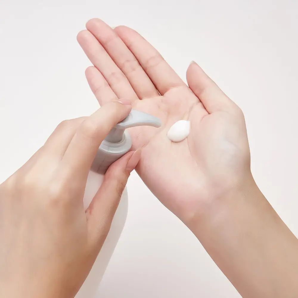 Mani che tengono una bottiglia di lozione e una piccola quantità di crema nel palmo.