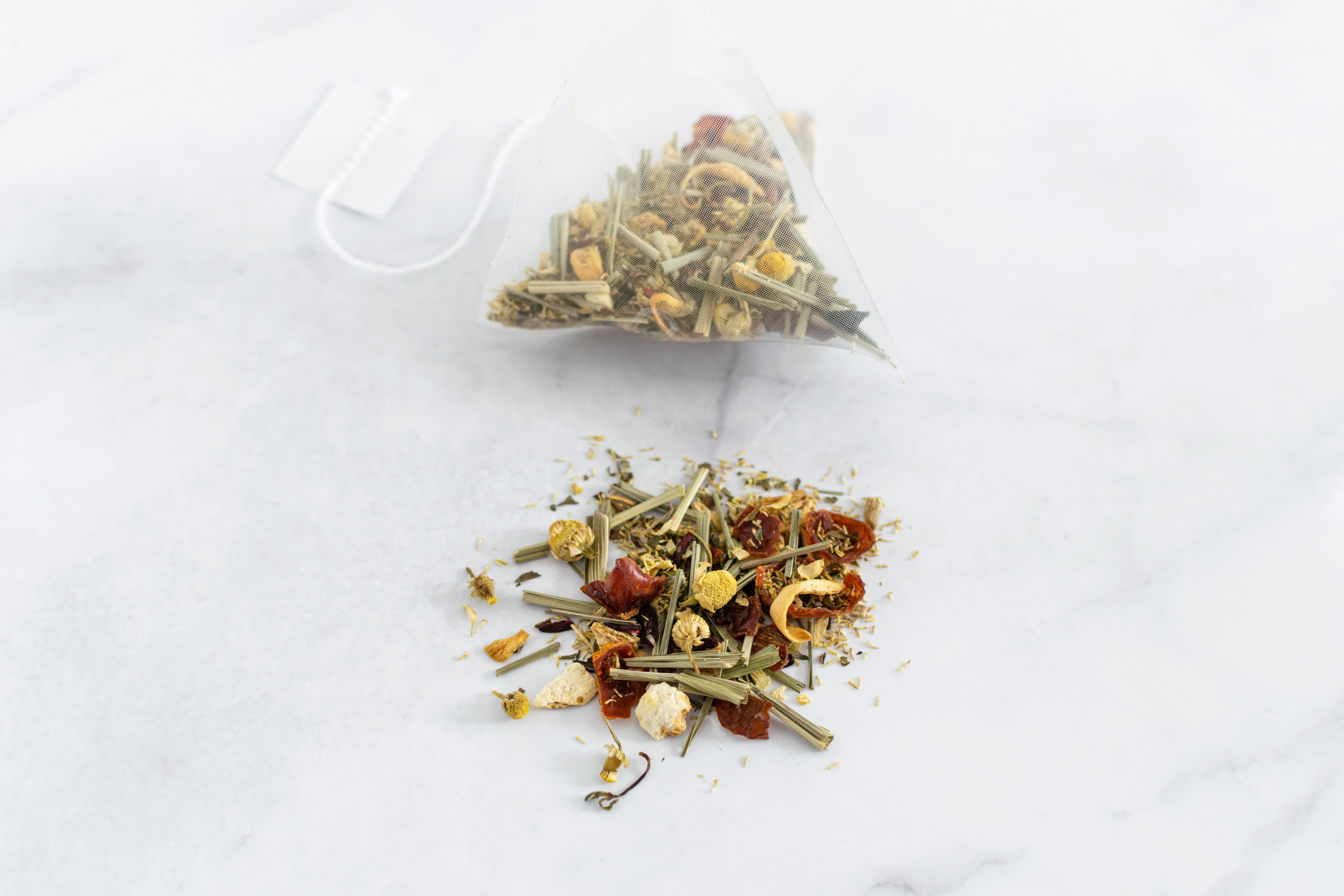 Bustina di tè trasparente con erbe e erbe sfuse. Etichetta attaccata. Su sfondo bianco.