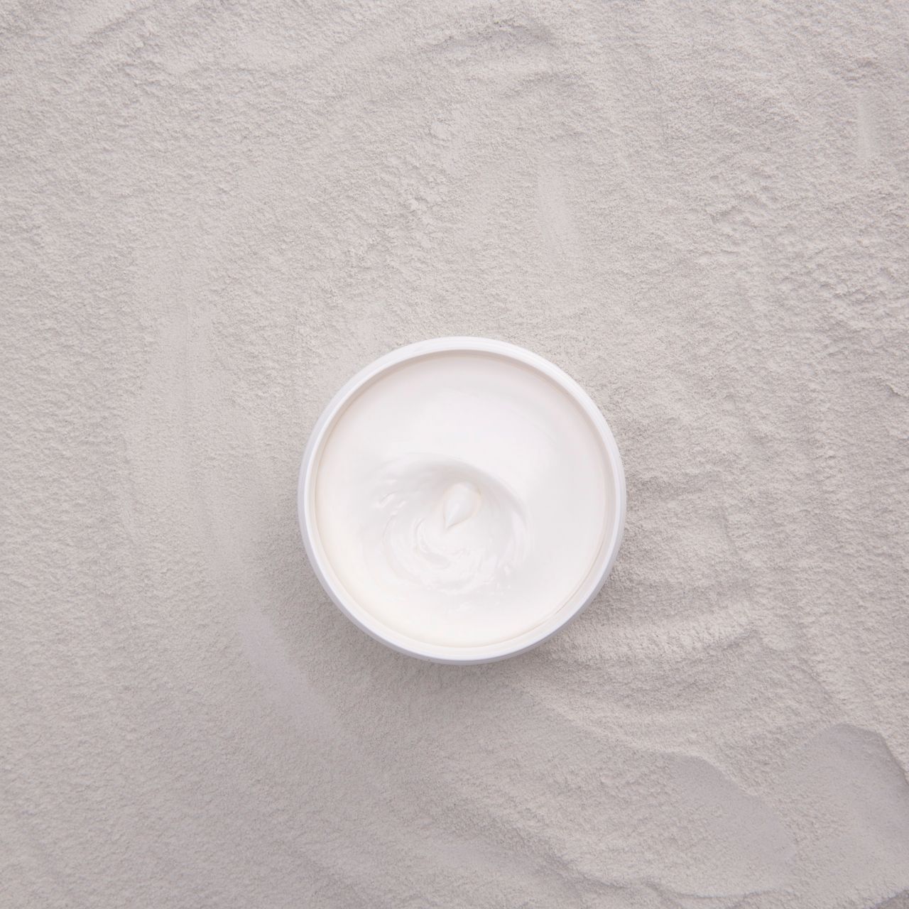 Una crema bianca in un contenitore aperto su sfondo sabbioso.