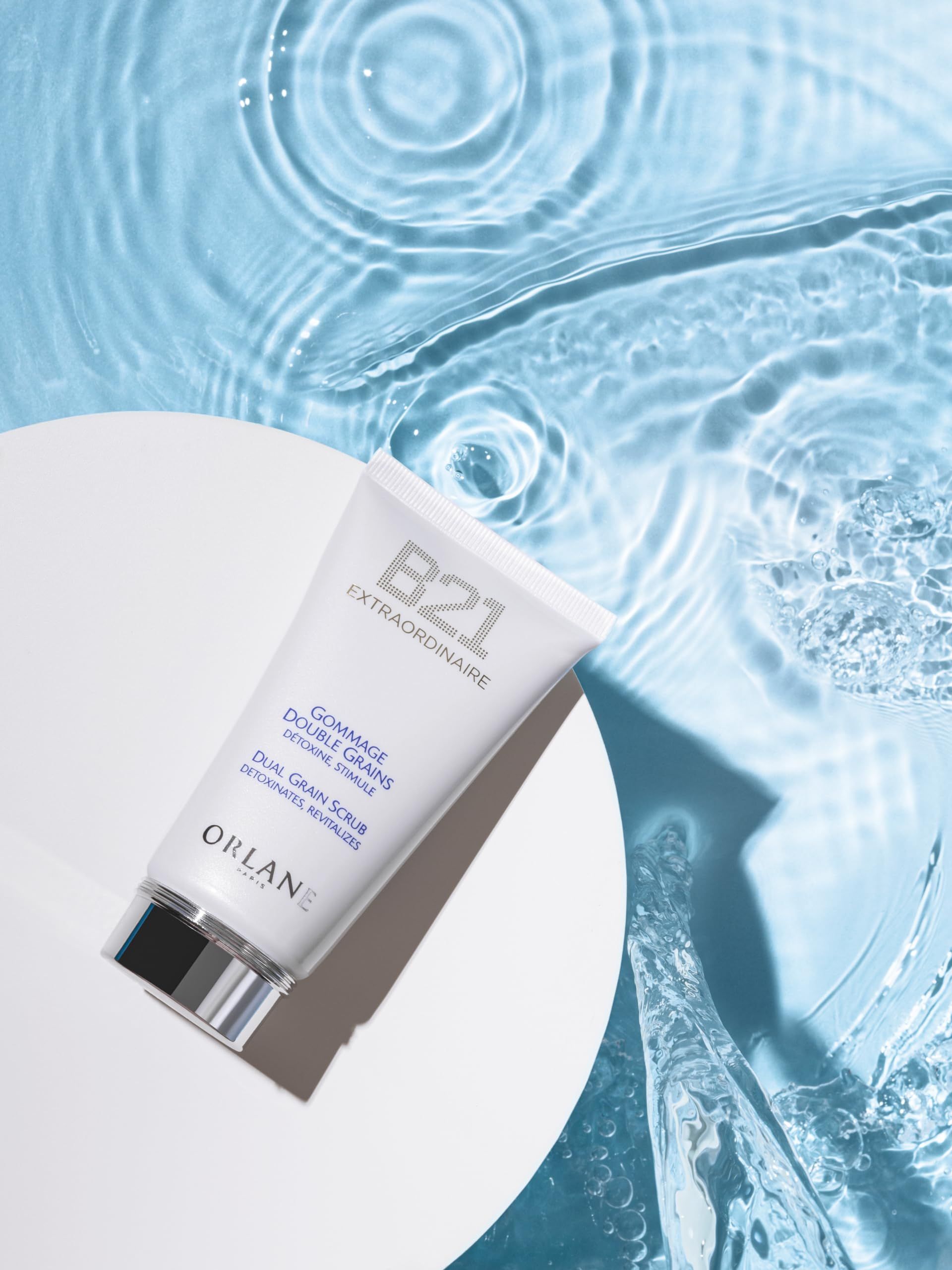 Tubo bianco con scritta 'B21 Extraordinaire' e 'Gommage Double Grains'. Su sfondo d'acqua.
