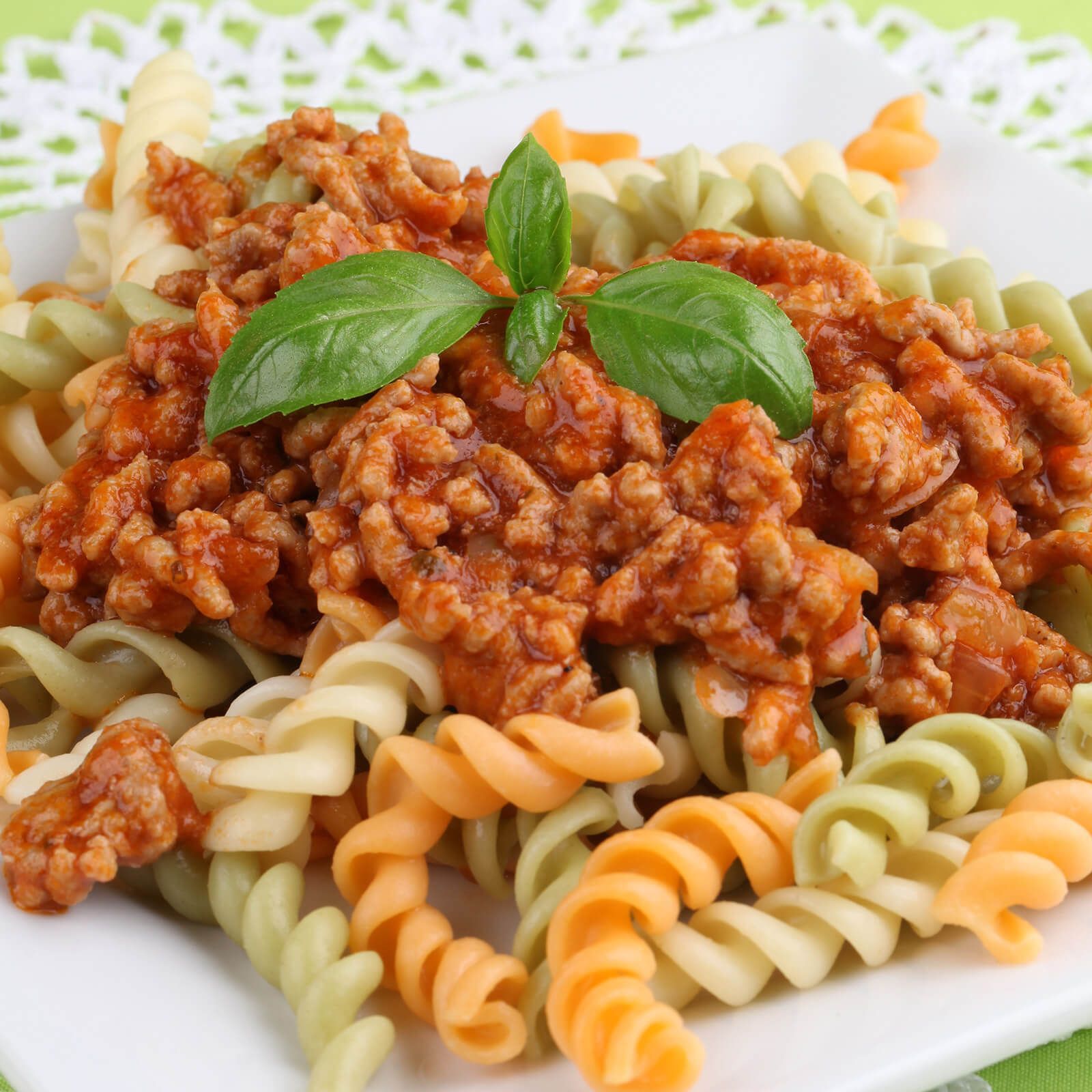 Piatto di fusilli tricolore ricoperti di ragù e foglia di basilico. Pasta gialla, rossa e verde.