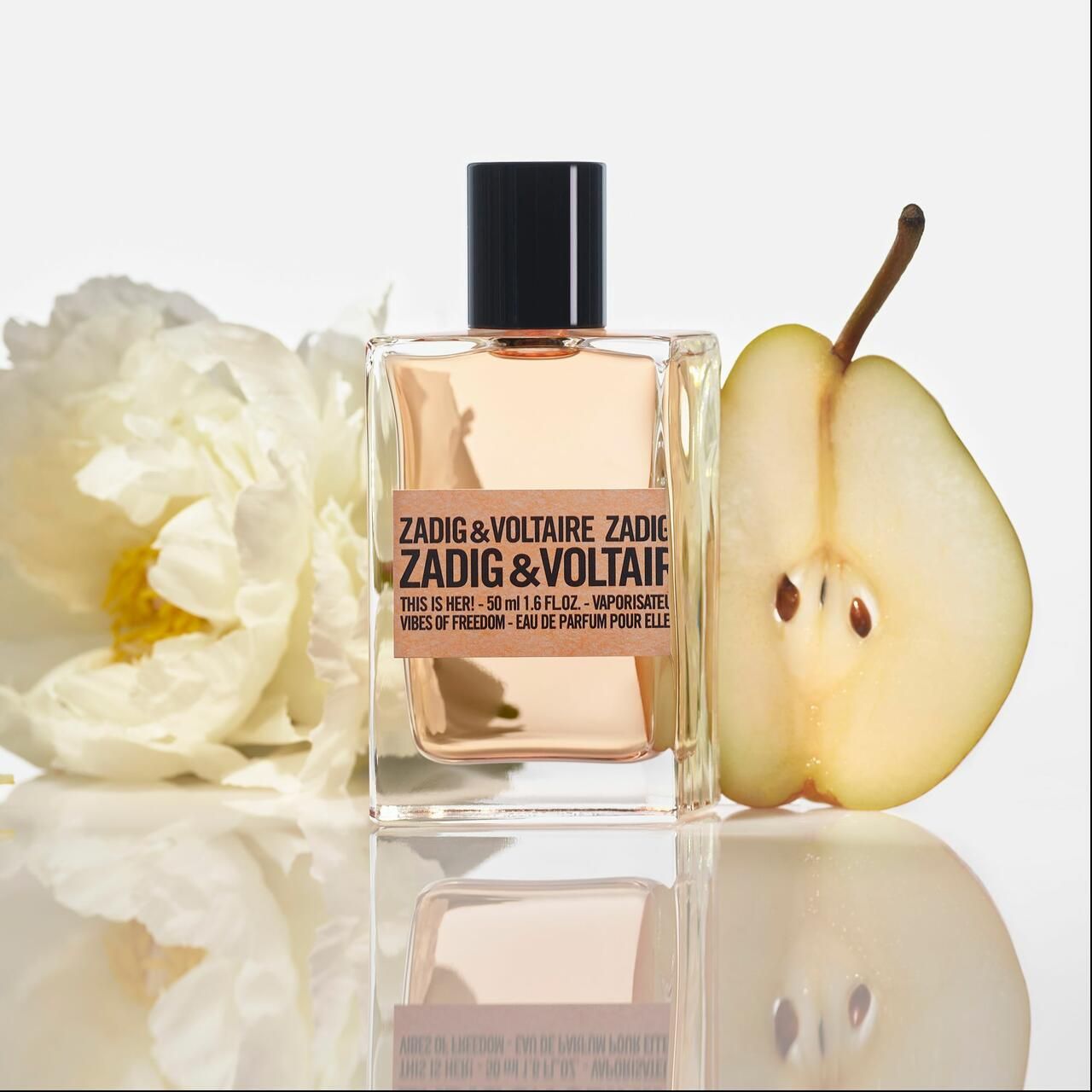 Flacone di profumo Zadig & Voltaire. Accanto a una pera e un fiore bianco.