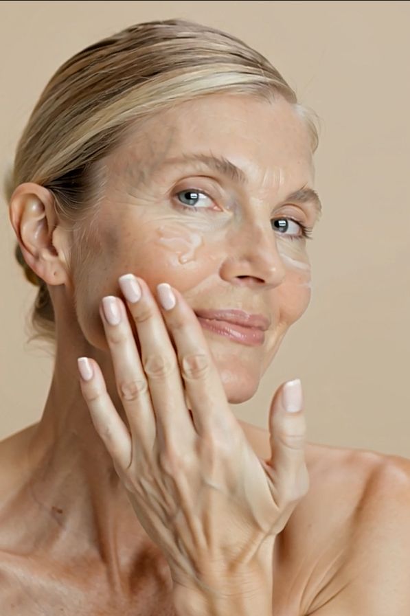 Donna che applica la crema sul viso. Sorride. Crema visibile sulla pelle.