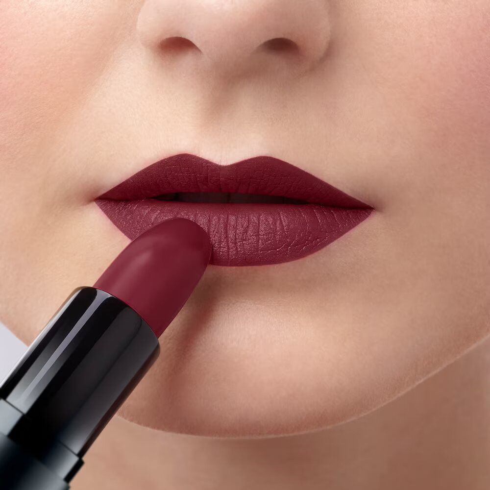 Persona che applica il rossetto sulle labbra. Rossetto bordeaux. Primo piano.