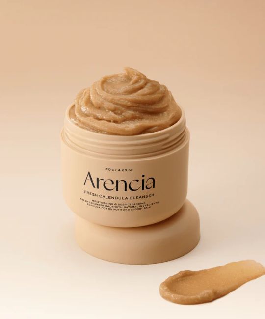 Crema beige in un barattolo aperto. Scritta: Arencia, Fresh Calendula Cleanser. Accanto, una noce di crema.
