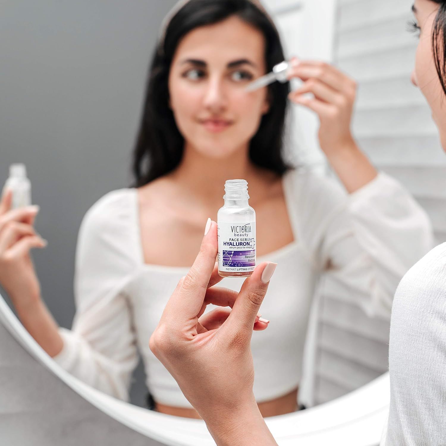Una donna tiene un flacone di siero davanti a uno specchio. Sul flacone si legge "Victoria Beauty Hyaluron+". Sta usando la pipetta.