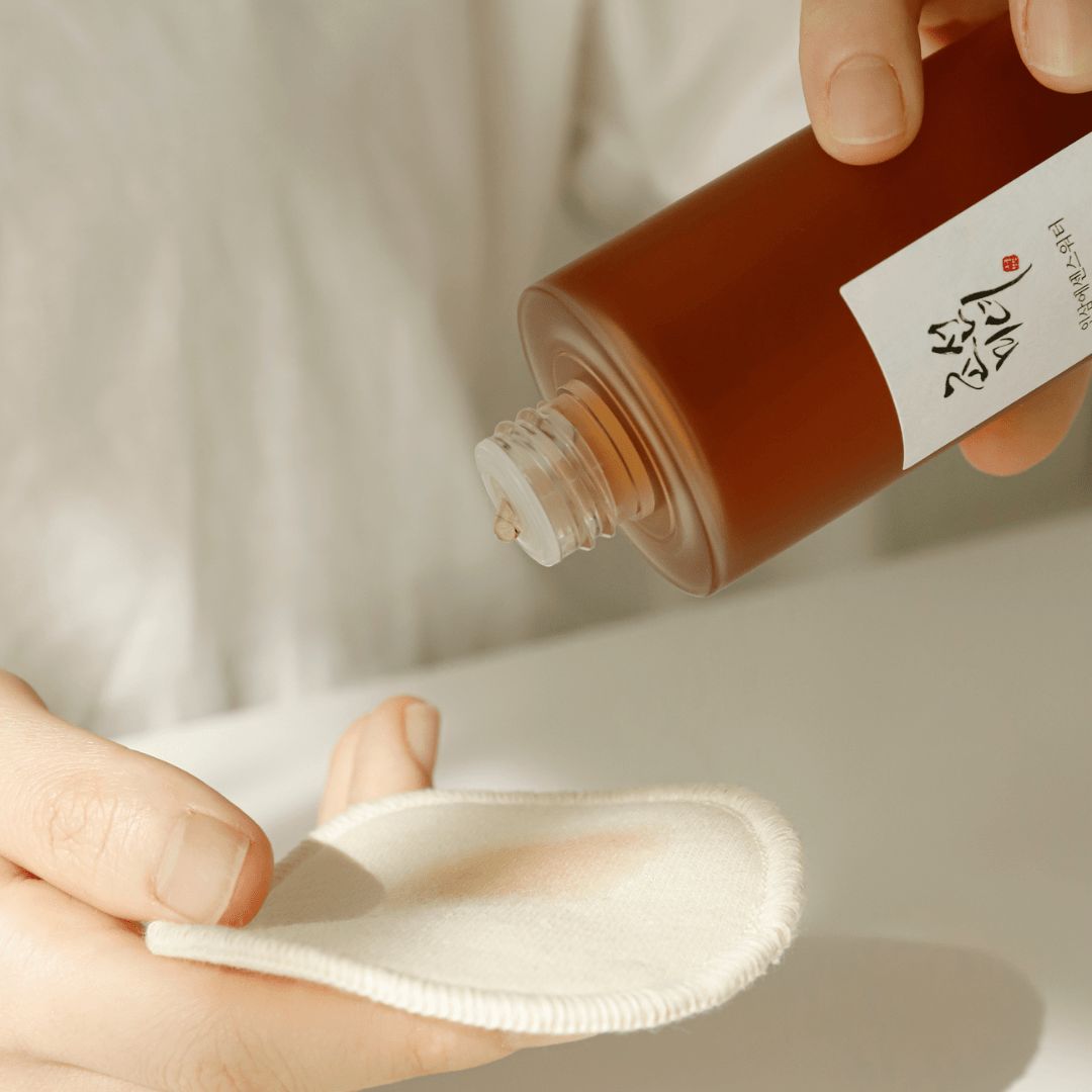 Mani che tengono un flacone e un dischetto di cotone. Liquido versato sul dischetto. Flacone con etichetta.