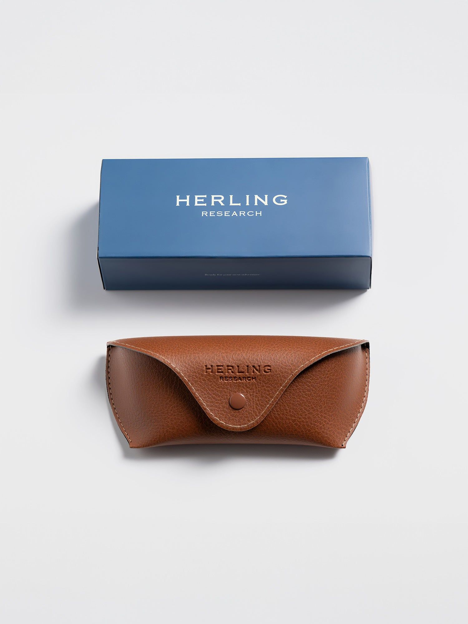 Scatola blu e custodia marrone. 'HERLING RESEARCH' sulla scatola. 'HERLING' in rilievo sulla custodia.