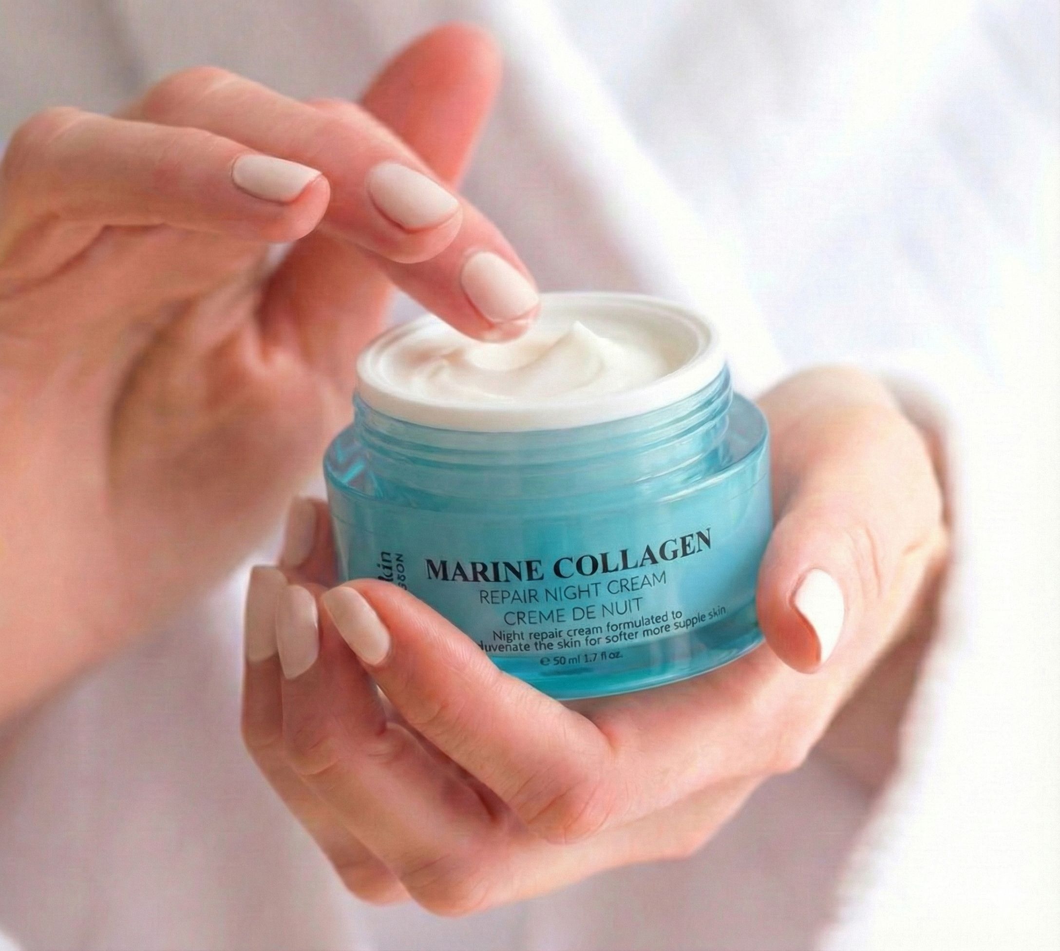Mani che tengono un vasetto di crema notte Marine Collagen. Crema prelevata con il dito. Vetro blu, coperchio argentato. Testo: Marine Collagen.