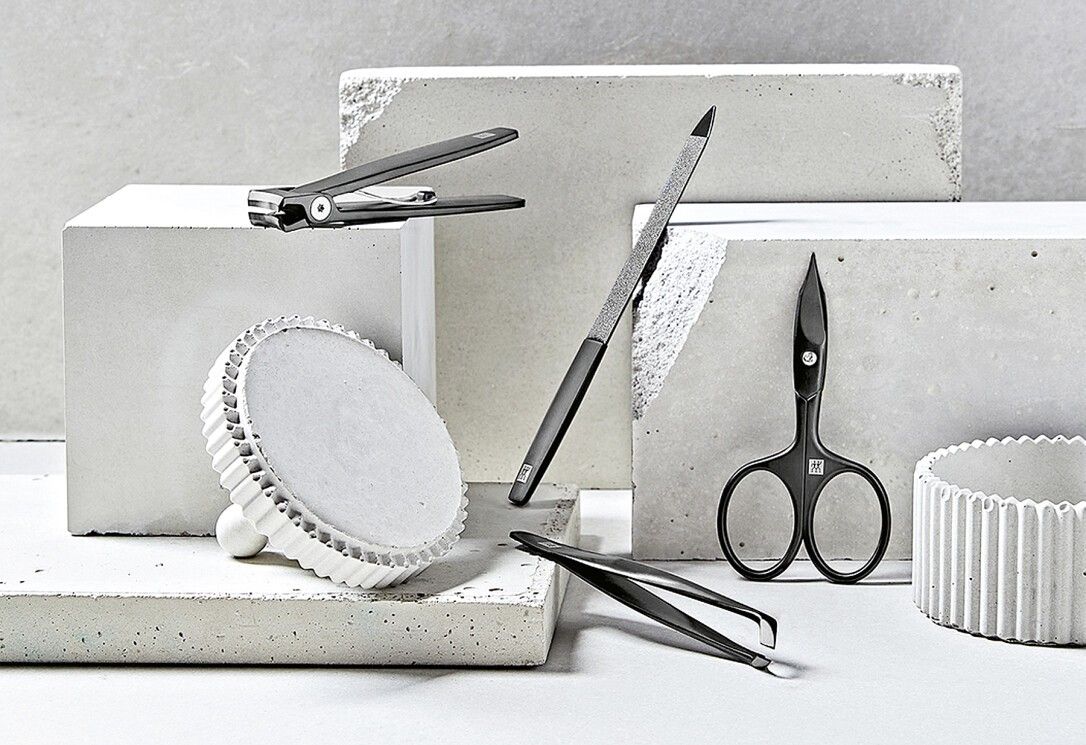 Vari strumenti per manicure, tra cui un tagliaunghie con logo ZWILLING. Posizionati su blocchi di cemento.