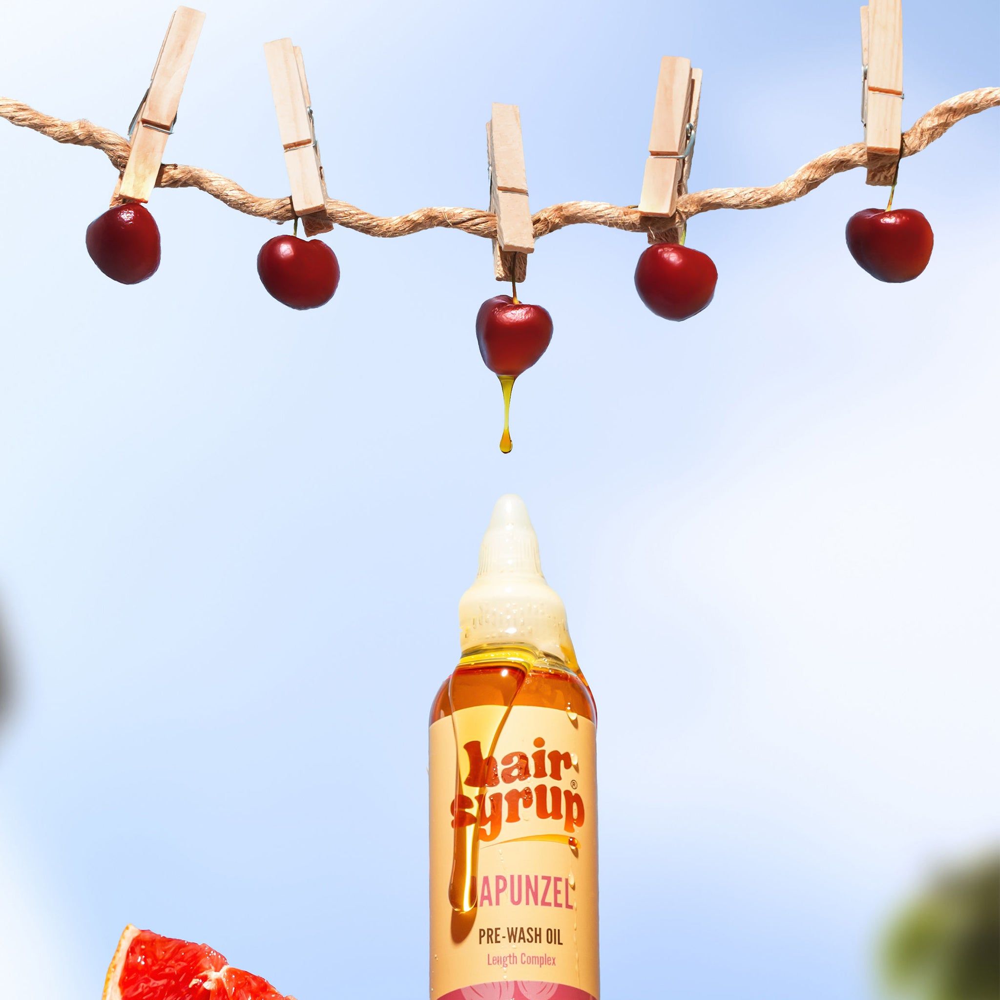 Bottiglia Hair Syrup Rapunzel Pre-Wash Oil con ciliegie su uno spago. Sfondo rosso.