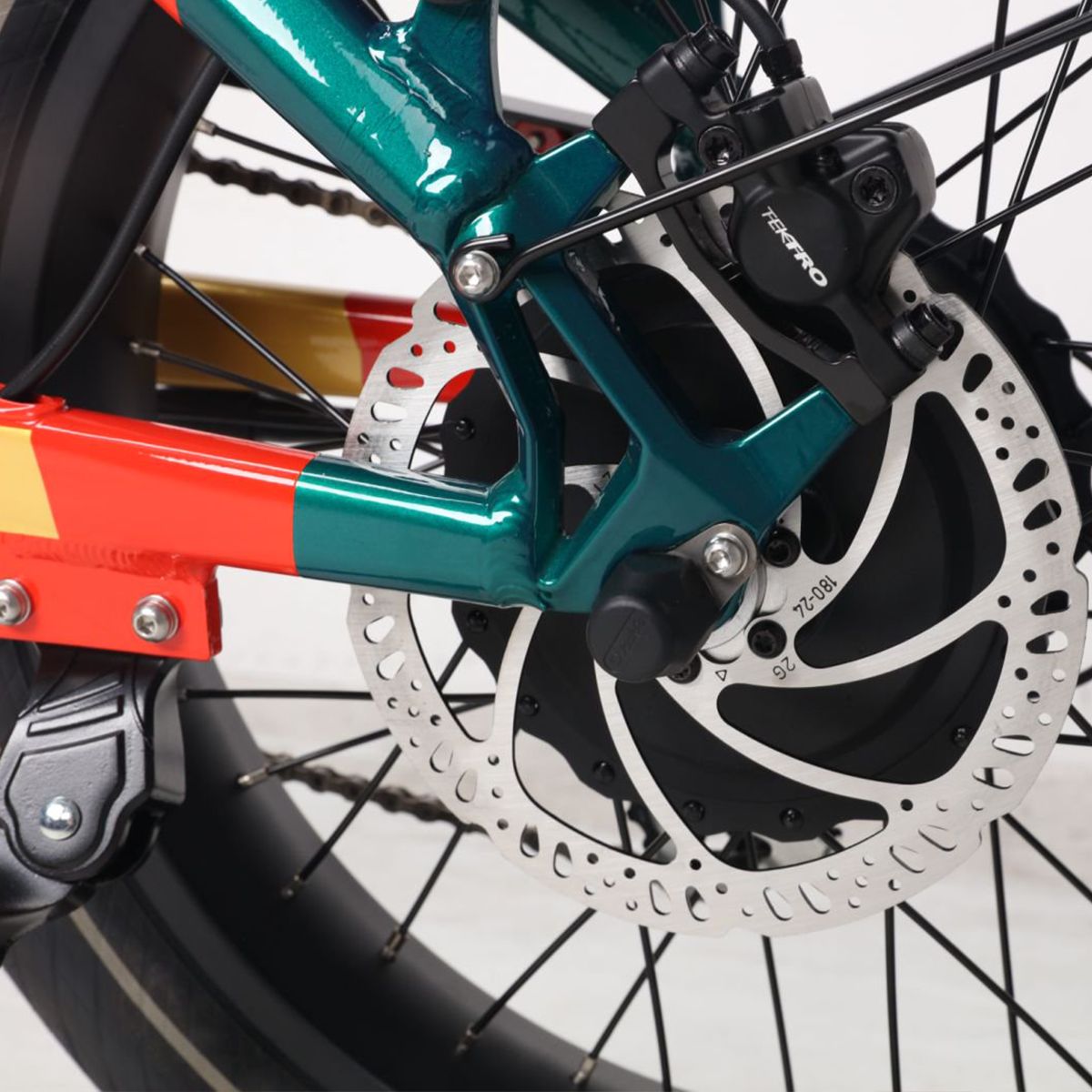 Freno posteriore di una e-bike. Freno a disco, dettagli neri. Design verde-rosso. Logo TEKTRO visibile.