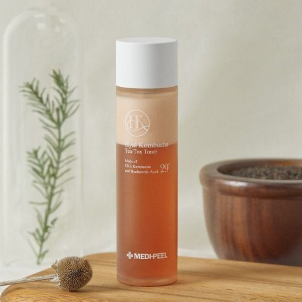 Flacone Hyal Kombucha Tea-Tox Toner su tagliere di legno, vicino a piante e ciotola.