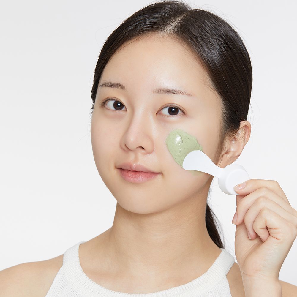 Donna con maschera sul viso. Una spatola applica la maschera verde.