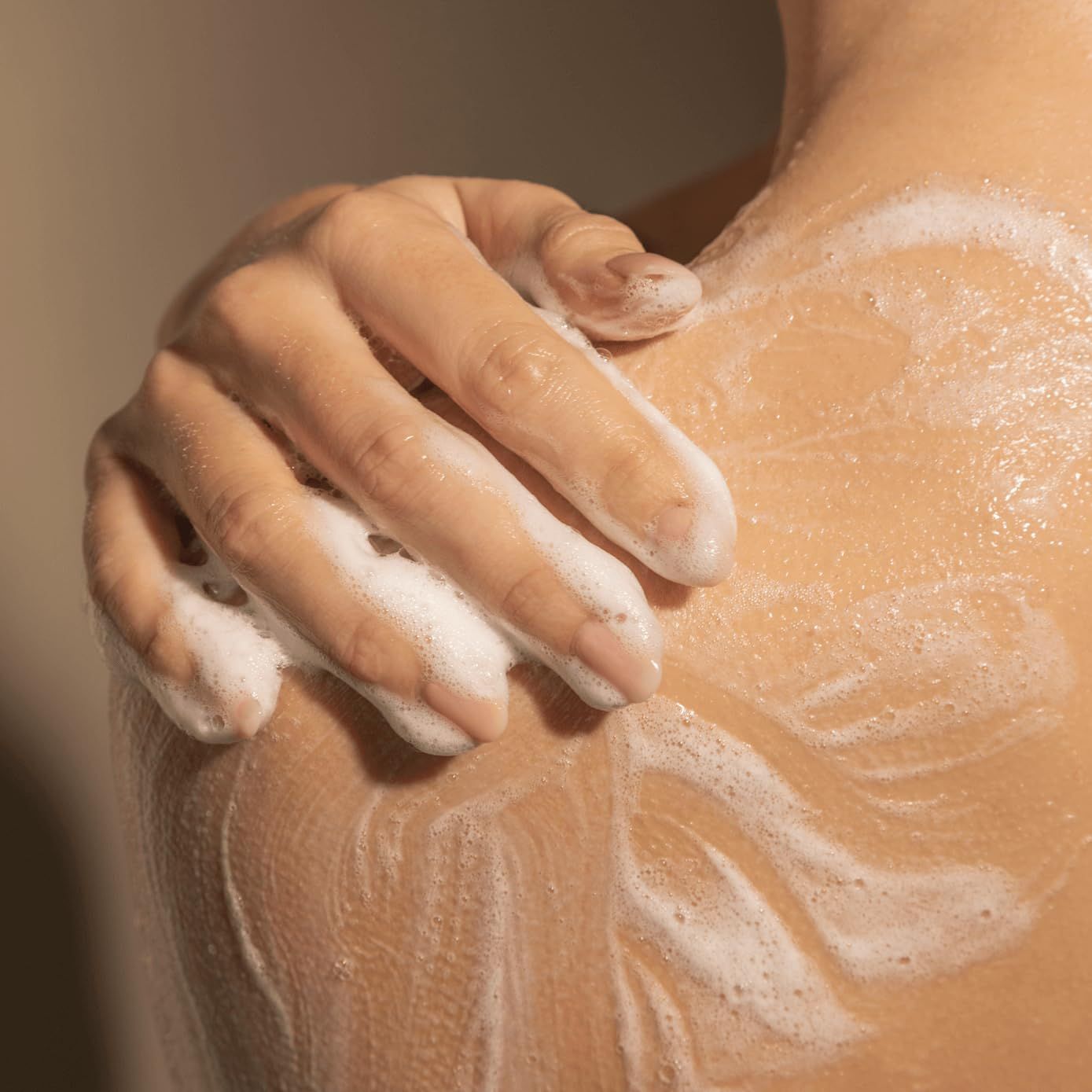 Primo piano di una mano che applica sapone su una spalla. Schiuma sulla pelle.
