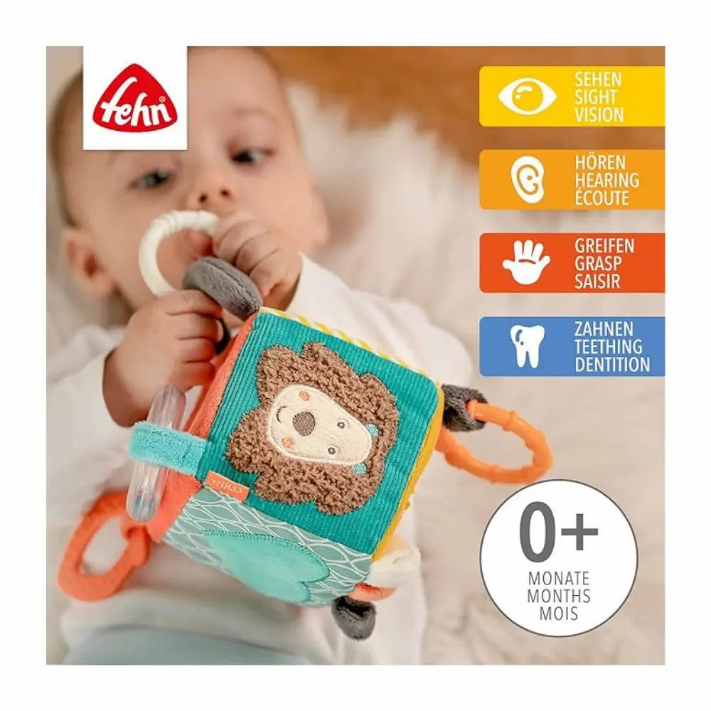 Bambino tiene cubo di stoffa con motivo leone. Marchio 'Fehn' visibile. Indicazioni su vista, udito, presa, denti. Età: 0+ mesi.