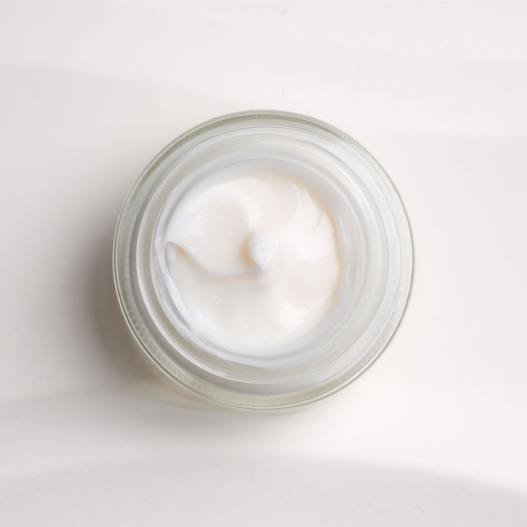 Crema bianca in vasetto di vetro. Vista dall'alto. Consistenza cremosa. Vasetto scanalato.
