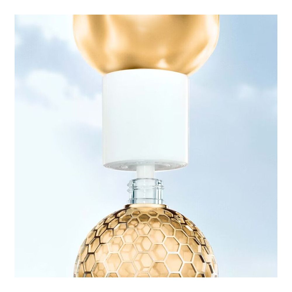 Flacone dorato con motivo a nido d'ape. Chiusura bianca in fase di montaggio. Bottiglia di vetro.