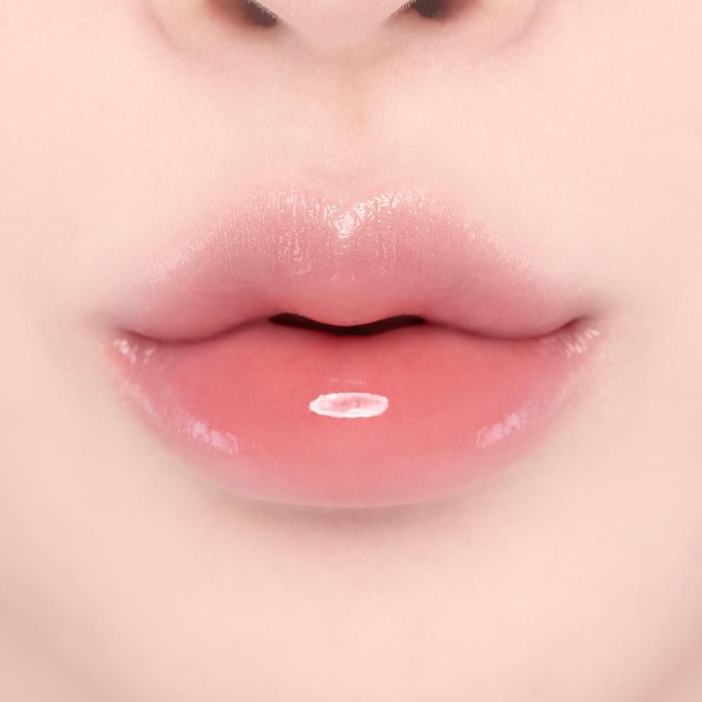 Primo piano di labbra piene e rosa con un lucidalabbra brillante e un punto luce bianco.