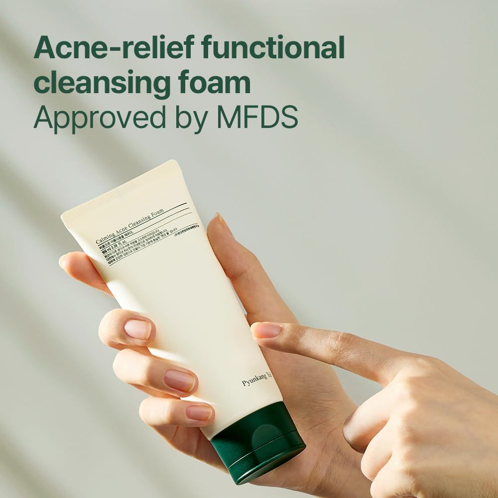 Mano che tiene un tubo di schiuma detergente. Corpo bianco, tappo verde. Testo: Acne-relief functional cleansing foam, MFDS.